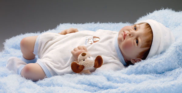 “Puppy Tails,” sculpted by Kymberli Durden, sports a cream velour playsuit with light blue stars, edge binding, cap and booties. The embroidered detailing includes a little puppy and the words best friends. The doll, 19 inches tall, has human hair and handset blue eyes that invite you to pick him up for a warm cuddle. A plush puppy rattle keeps him happy.