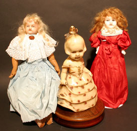 An early wax doll flanked by two porcelain dolls