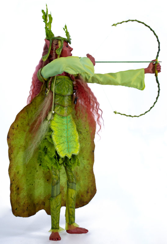 Marian, 19 inches, is based on a walking leaf (family phylliidae). Of all forms of camouflage found in nature, this insect is one of my favorites. Such a stealthy faery could only be an archer, and it seemed fitting to name her after Maid Marian from the Robin Hood legends. Her armor, crown, and bow are 3D printed and painted with acrylics, and her cape is made of leather lined with silk taffeta. Other elements of her clothing are made from silk, wool, tulle, and faux leaves. She has glass eyes and wool hair.
