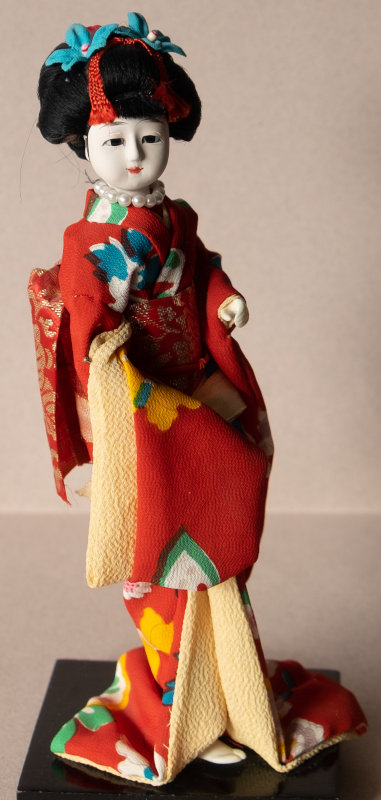 Although I haven’t been to Japan, my husband did a photographic tour there, so I had to add this exquisite geisha doll as one of the most recognizable dolls symbolizing Japan. She is about 8 inches tall and made of porcelain with inset glass eyes, hallmarks of a very well-crafted geisha doll. She is dressed in a beautiful silk kimono in colors worn in high summer or fall. The significance of the string of pearls eludes me, although probably refers to Japan’s famous cultured pearls. I found her in an opportunity shop [a thrift store, usually run for a charity] — always a good place to start looking for unusual dolls.