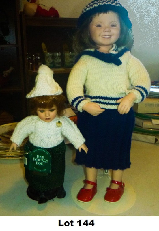 Lot 144 is these two dolls: a 12-inch Irish Heritage doll tagged “Clodagh” and a bisque-head doll marked “MIP 3602” in knitted sailor dress with hat, displayed on stand.