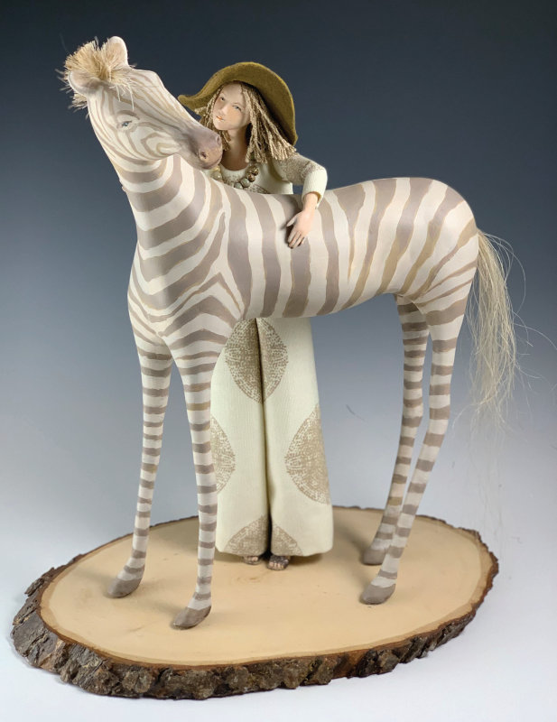 Embracing Her Essence by Cindee Moyer. Figure of a woman with her arm across the back of a zebra with exaggerated long legs.