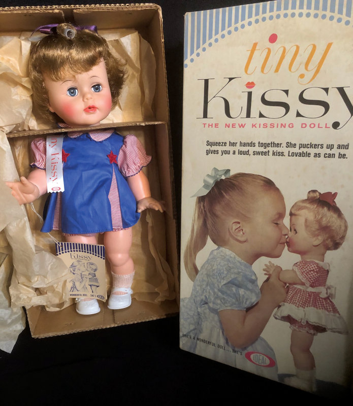 Photo of 1963 Tiny Kissy doll in open box. Box top is shown at right.