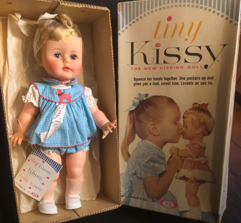 Photo of Tiny Kissy doll in open box, with box top next to it. The basic Tiny Kissy doll was available in various hair colors and fashions.