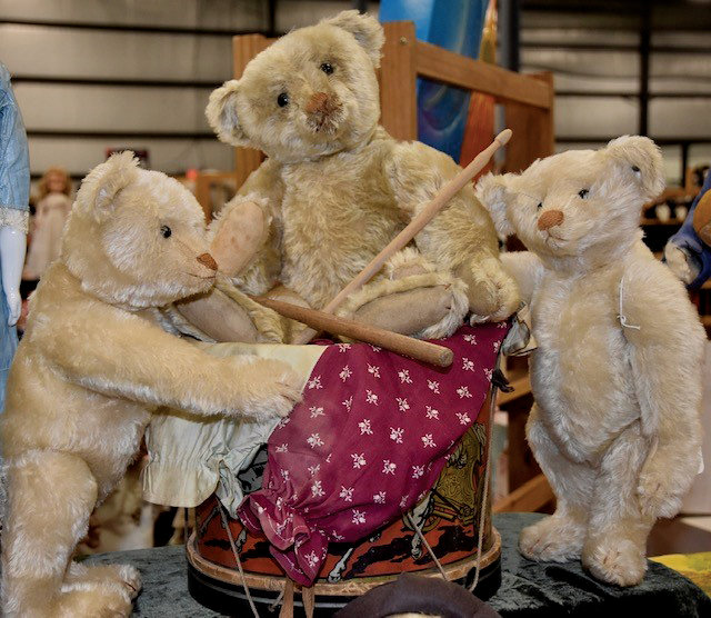 Three teddy bears; the center bear sits on a toy drum.