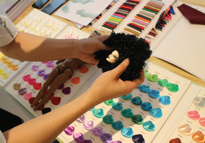 Huadong holds a sample of curly nylon fiber behind a dolls head to evaluate the effect.