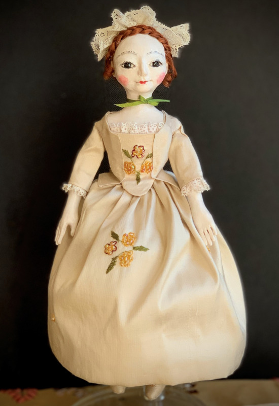 Charlotte is an 8-inch Queen Anne-inspired art doll made to be held by a larger doll or displayed on her own. Her polymer clay body has hinged legs, so she can sit. Her clothing is made from silk and French vintage lace, with a cotton petticoat and bloomers, silk shoes, a vintage lace cap, and a red mohair wig.