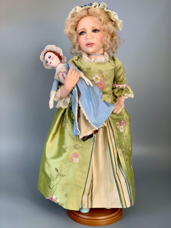A child of the 18th century, 16-inch Patience holds a Queen Anne doll and wears a dress made with embroidered silk trimmed with vintage lace. Her shoes are blue silk with handmade rhinestone buckles.