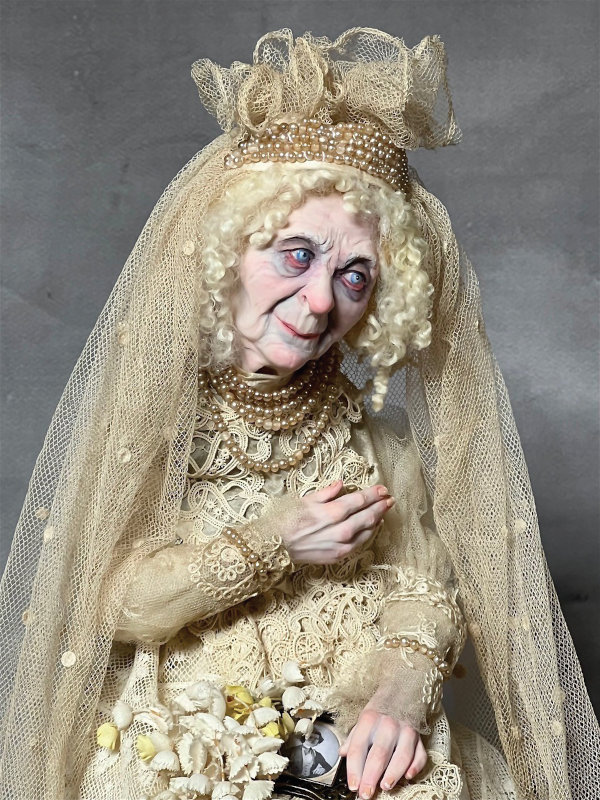 Poor Ghostly Miss Havisham from Charles Dickens’ Great Expectations is a seated doll on an antique architectural wood base approximately 19 inches tall. She is dressed in antique laces and fine antique silks, antique water pearls, and satins.