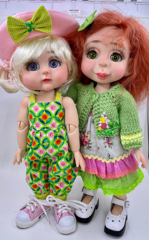 Two dolls side-by-side dressed in different outfits but using similar color combinations (green, white, yellow, pink).