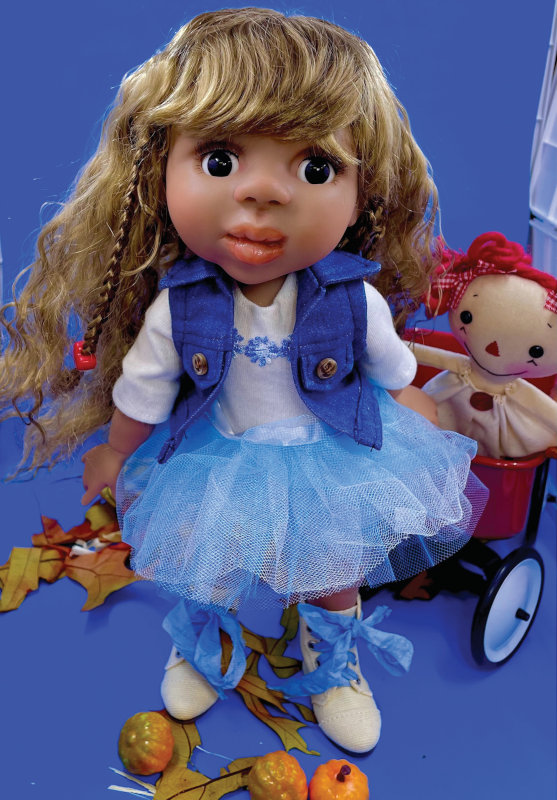 Doll in white and blue outfit pulls a red wagon with a cloth doll similar to Raggedy Ann inside.