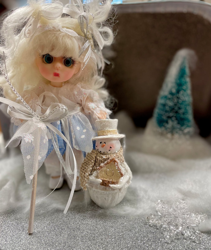 Doll dressed in fanciful outfit with a tiny snowman