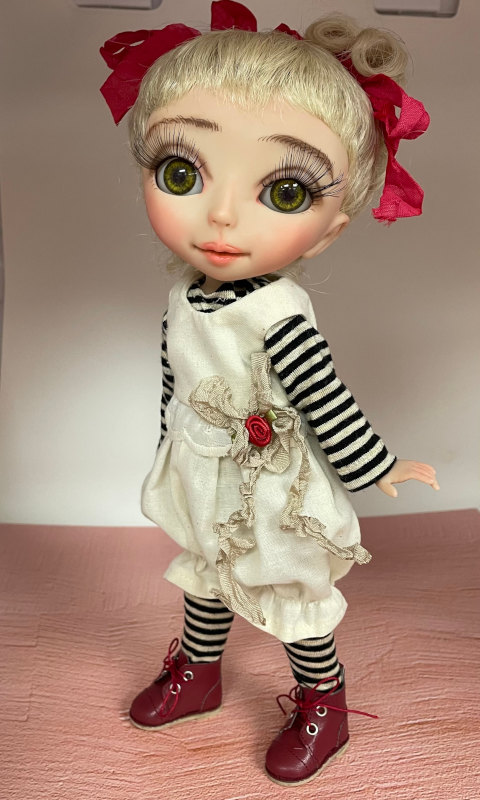 Doll with white dress over black-and-white striped top, striped socks and red-brown shoes.