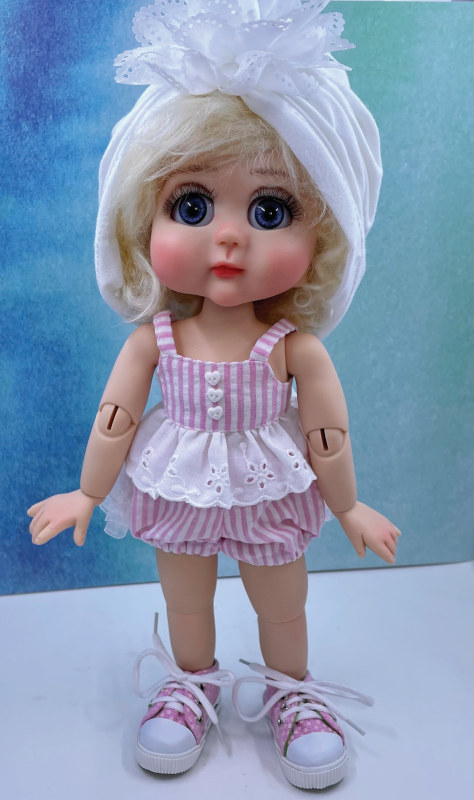 Toddler doll in pink and white dress and sneakers.