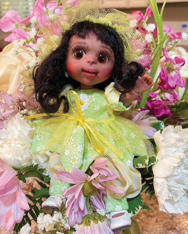Doll in a green floral print dress with yellow netting overlay and headpiece.