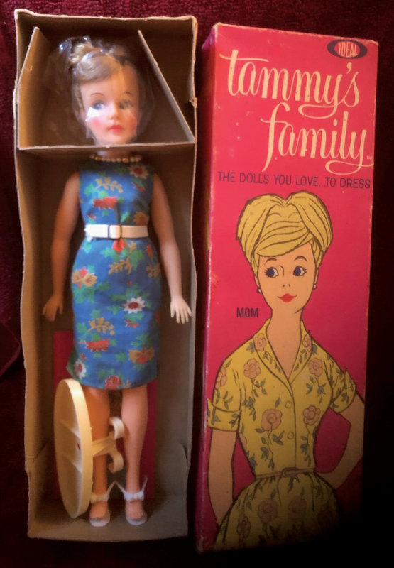 A doll still in the box wearing a belted dress and pearl necklace. The box top next to it reads "Tammy's Family: The Dolls You Love to Dress" and "Mum" next to the illustration of a woman.
