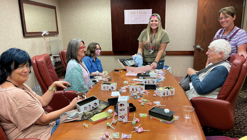 Several women gathered around a table looking at tiny ball-jointed dolls (BJDs)