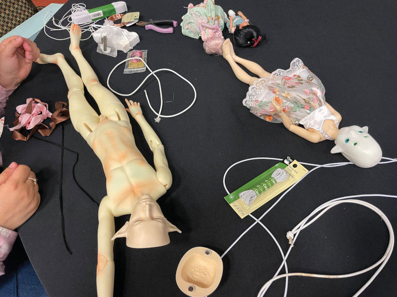 several BJDs on a table along with elastic, head caps, and other materials used for restringing.