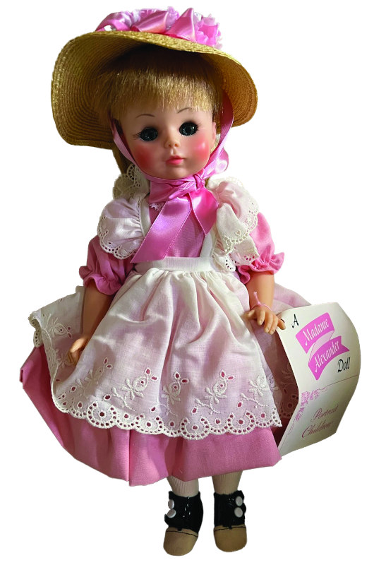 Doll wearing a pink and white dress with straw hat, with a wrist tag showing.