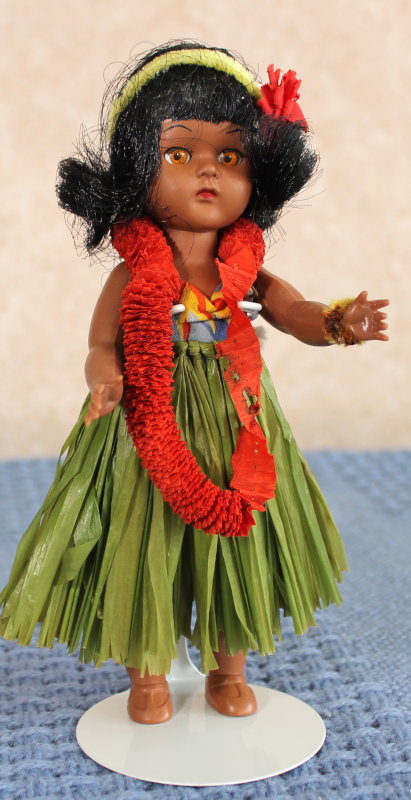 A brown-skinned doll wearing a Hawaiian outfit, including "grass" skirt and lei.