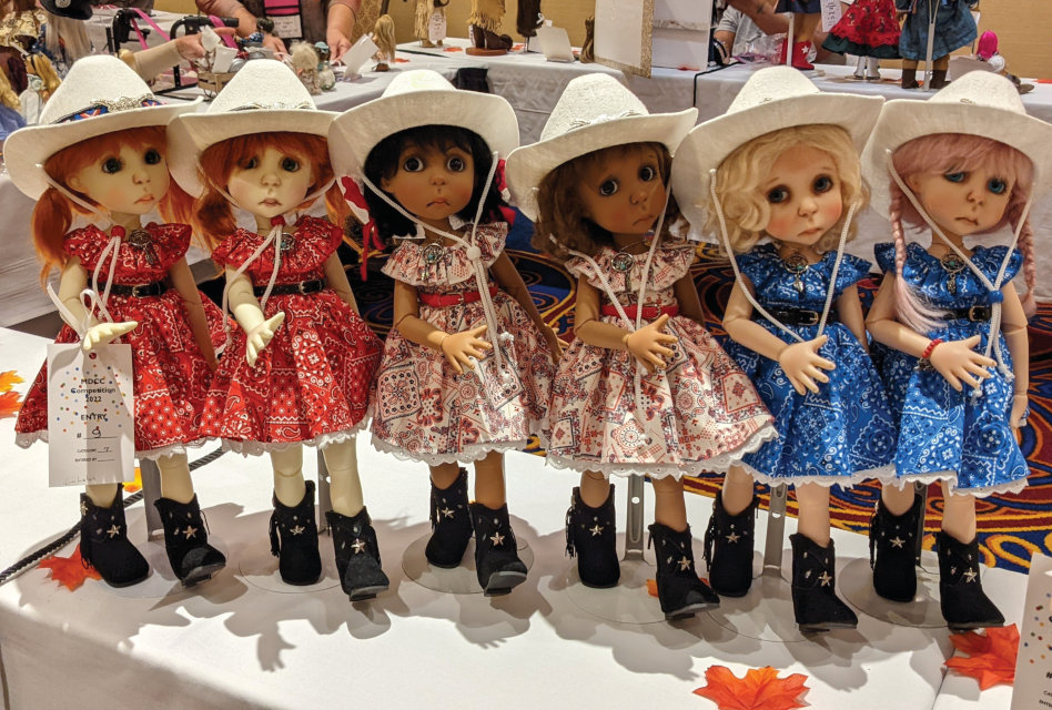 Six BJDs posed as if line dancing. They're all wearing white cowboy hats and black cowgirl boots. The two on the left wear red bandana-print dresses, the center two wear white bandana print, and the two on the right have blue bandana-print dresses.