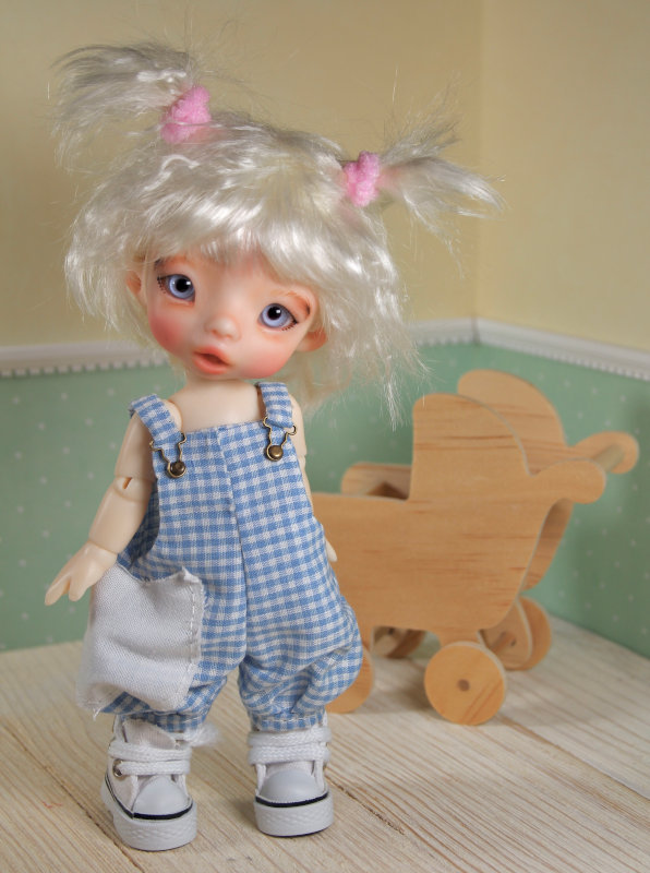 BJD of a blond girl in pigtails wearing blue checked overalls and white sneakers.