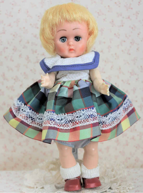 Plastic doll with short blond hair in a dress with white bodice and plaid skirt.