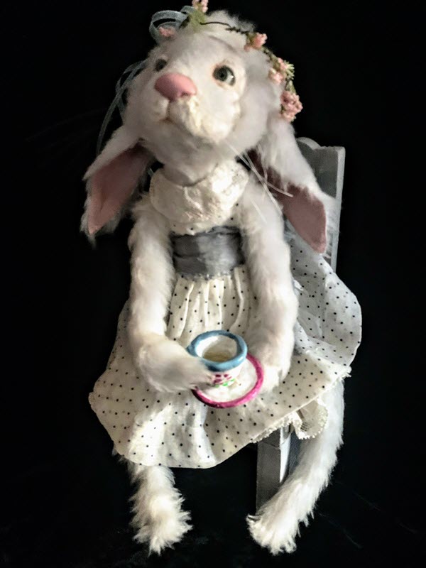 White rabbit wearing a polka-dot dress and flower crown hold a teacup while sitting down