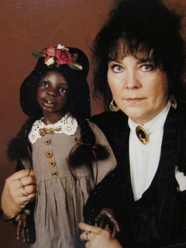 Doll artist poses while holding a doll with a dark-brown skin tone