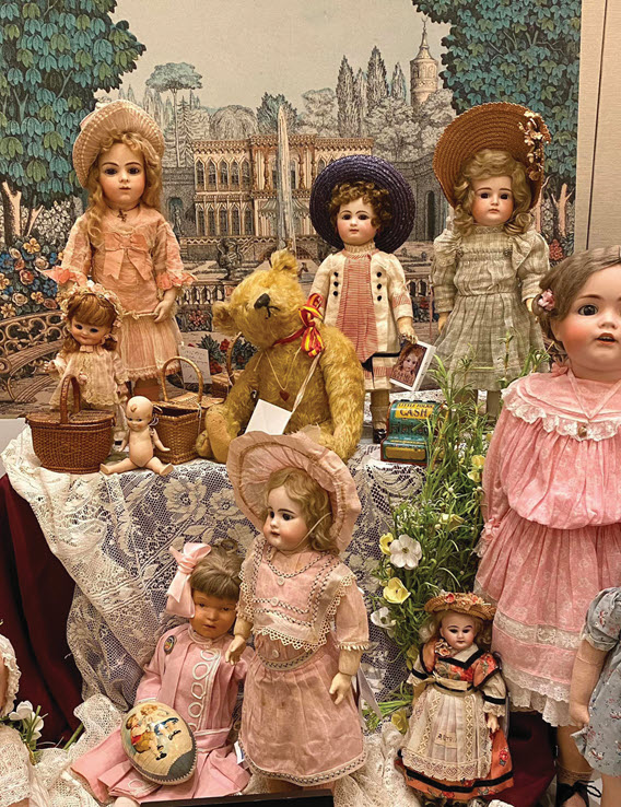 An assorted collection of antique dolls and accessories displayed on a table in front of a backdrop