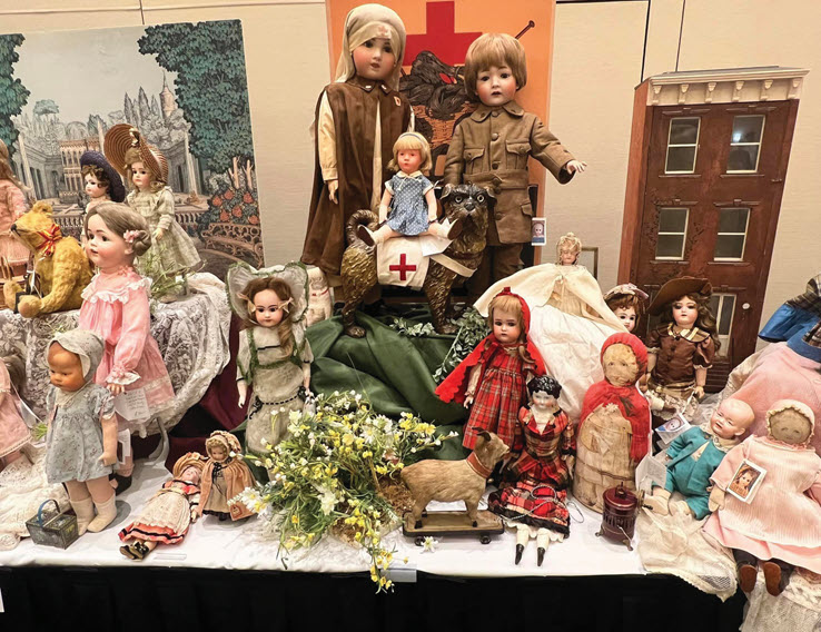An assorted collection of antique dolls and accessories displayed on a table, including military-themed dolls