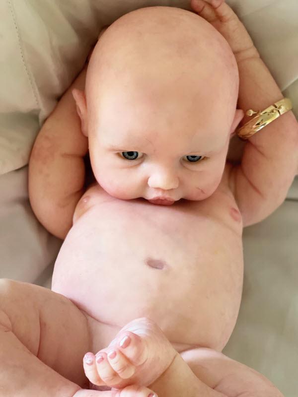 An baby doll with no clothes on poses with crossed legs and arms behind the head.
