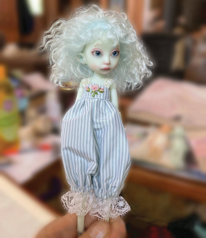 Pale blue doll with bluish hair wears a blue-and-white-striped jumper