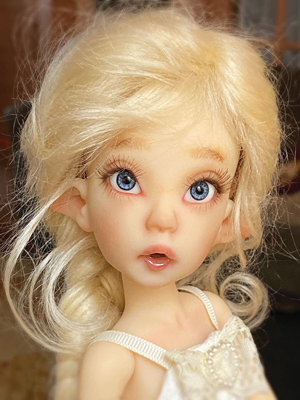 Doll has blue eyes, elf ears, and blond hair pulled back in a braid