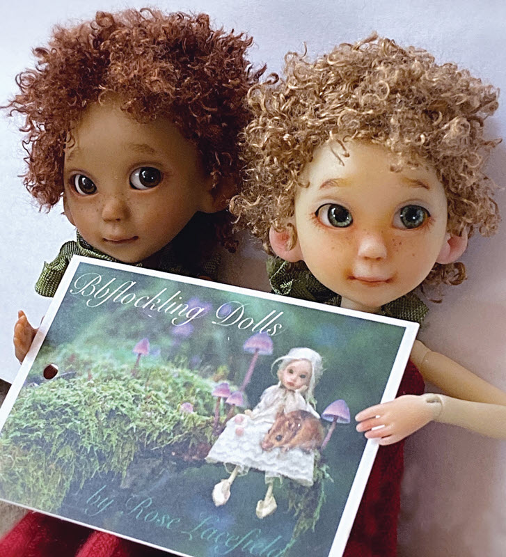 Two dolls, one with a pale skin tone and one with a brown skin tone, sit beside each other and hold a promotional photo