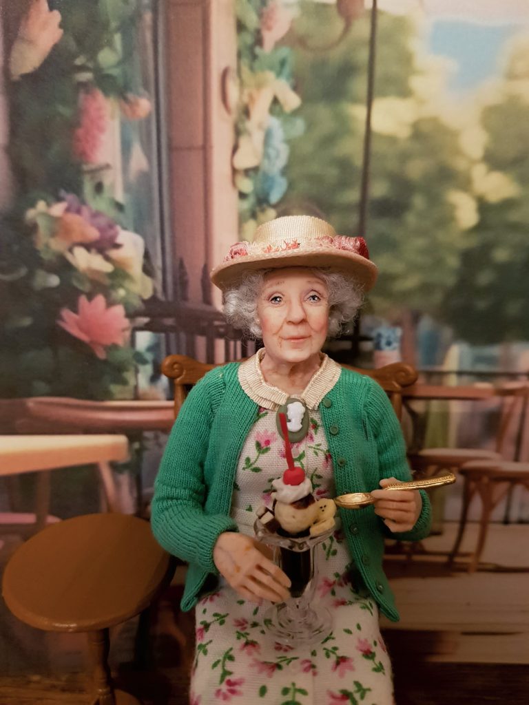 miniature doll elderly lady in a floral dress and hat with ice cream sundae