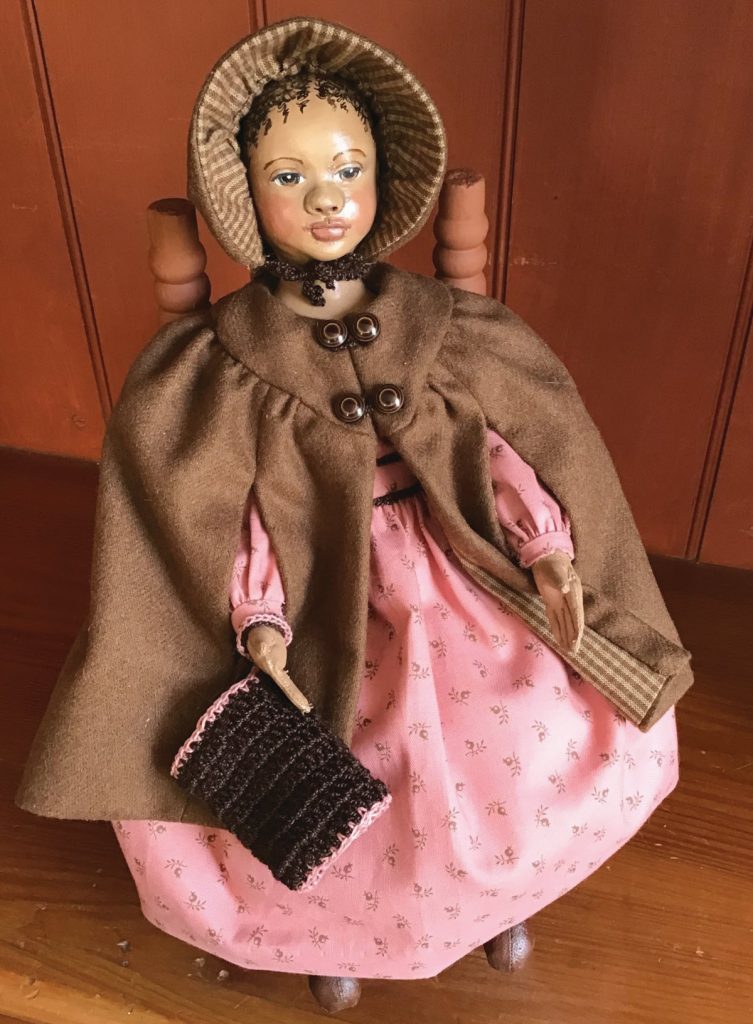 African American doll in pink dress and brown coat