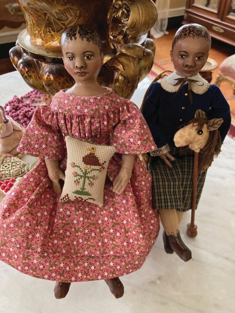 African American historic dolls. One in pink dress with embroidered pillow and one in plaid nickers and blue shirt with a pole horse