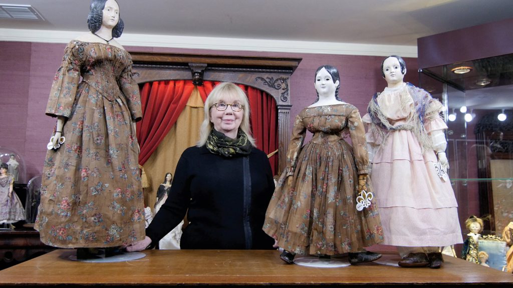 woman in black with three large antique dolls