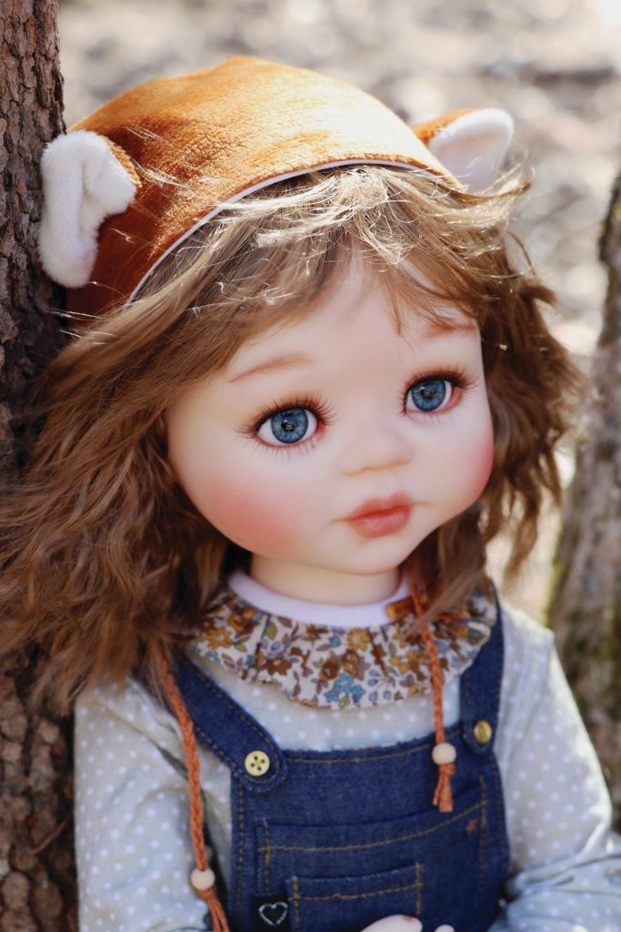 doll with brown hair, blue overalls and brown hat with ears